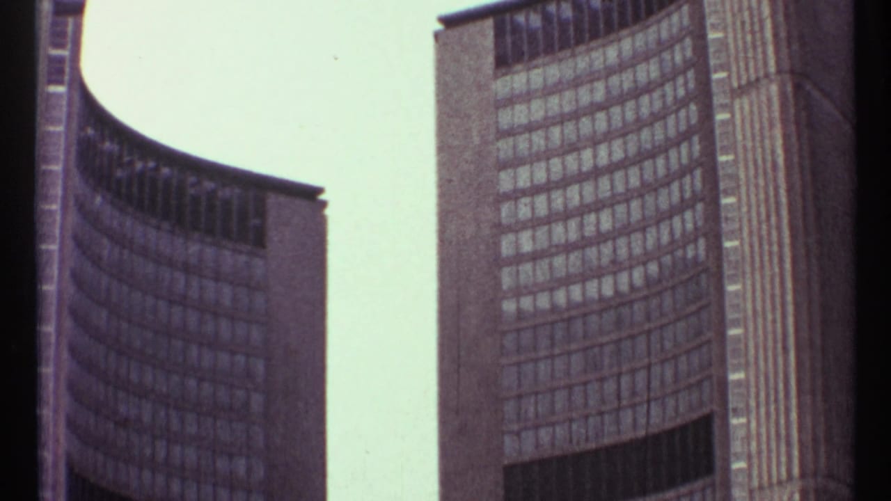 1967 Toronto 8mm frame showing curved modernist high-rise facades with repeating window grids and pale sky.