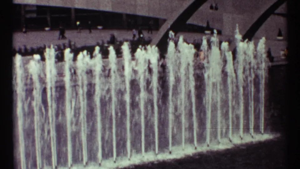The 8mm frame holds on dense vertical fountain sprays in Toronto, with background pedestrians and mid-century architecture.