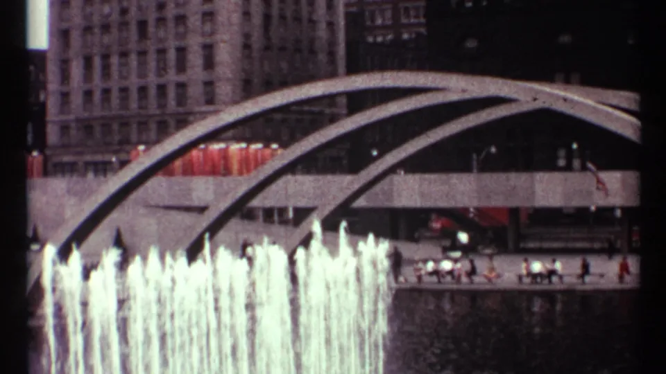 1967 Toronto exterior with bright fountain spray, arched concrete spans, distant pedestrians, cars, and office buildings.