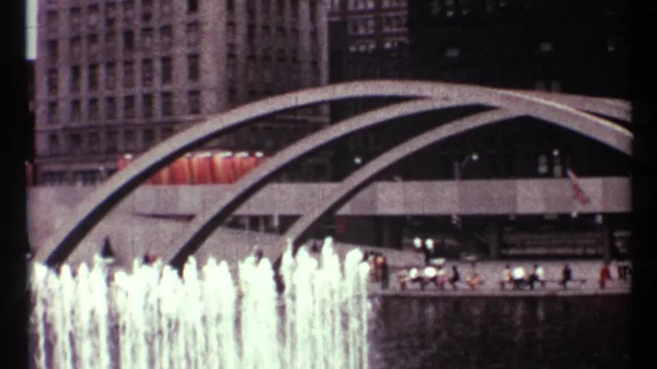 1967 Toronto frame with fountain jets in the foreground, concrete arches overhead, pedestrians on a walkway, and downtown buildings beyond.