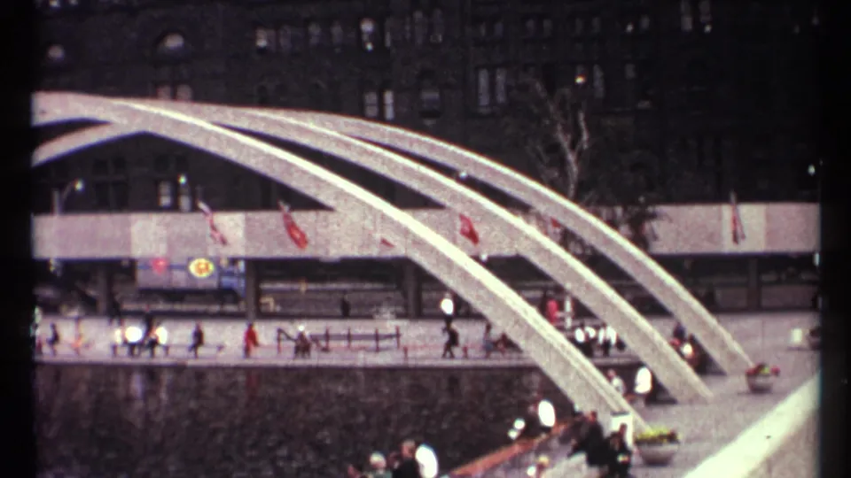 1967 Toronto home-movie view of concrete arches over water, people on the walkway, flags, vehicles, and dark building facades.