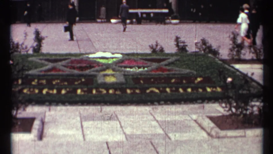 Toronto 1967 public-square view with a large floral display, pedestrians, benches, shrubs, and paved walkways.