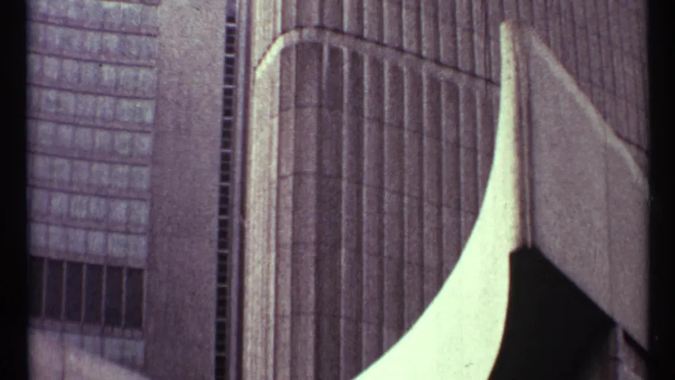 Toronto 1967 home-movie frame of a modernist building exterior, framed tightly on windows, vertical facade lines, and pale concrete curves.