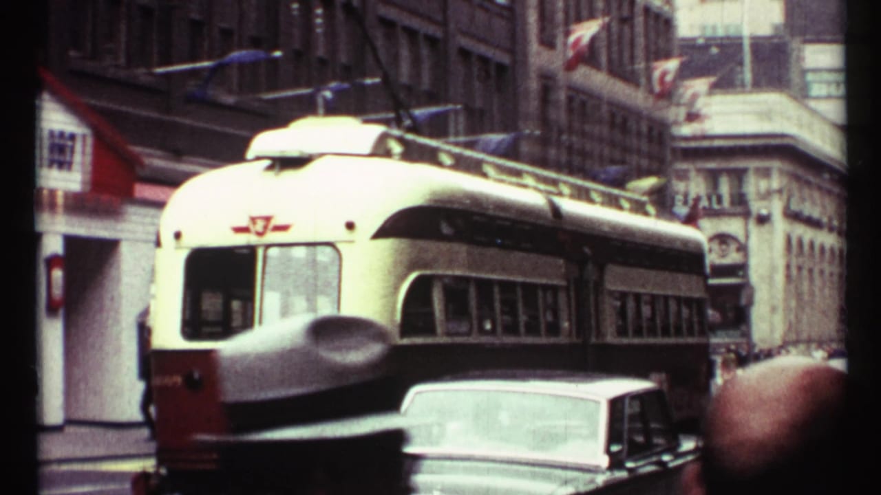 Red-and-white streetcar passes through city traffic near storefronts and flags.