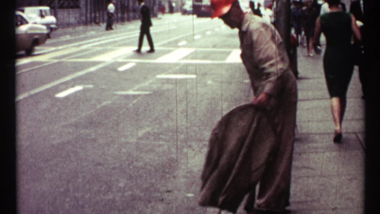 1967 Toronto street view with pedestrians, a marked crosswalk, road traffic, and a man bending near the curb in 8mm footage.