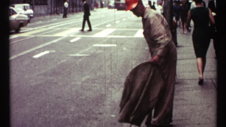 1967 Toronto street view with pedestrians, a marked crosswalk, road traffic, and a man bending near the curb in 8mm footage.