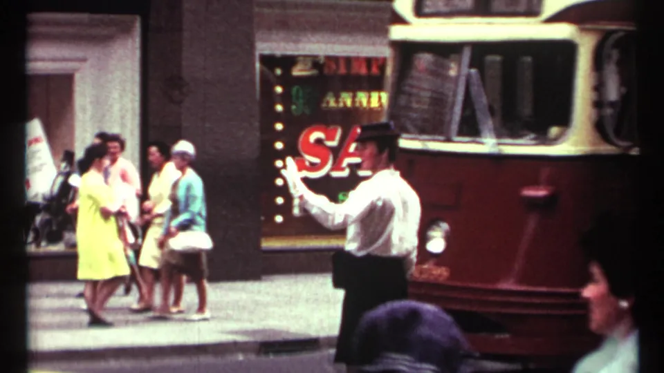 1967 Toronto sidewalk scene with a white-gloved traffic director, pedestrians in period clothing, and a red-and-cream transit vehicle.