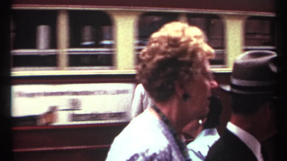 1967 Toronto street scene with pedestrians in period clothing passing in front of a moving streetcar or trolley.