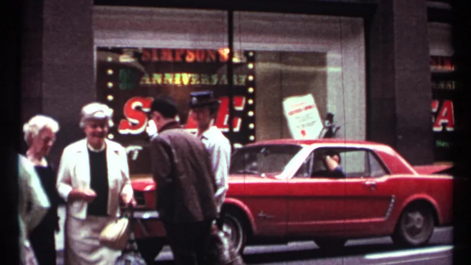 Pedestrians in 1960s clothing stand and walk near a red Mustang parked outside the Simpson's sale window on a Toronto street.