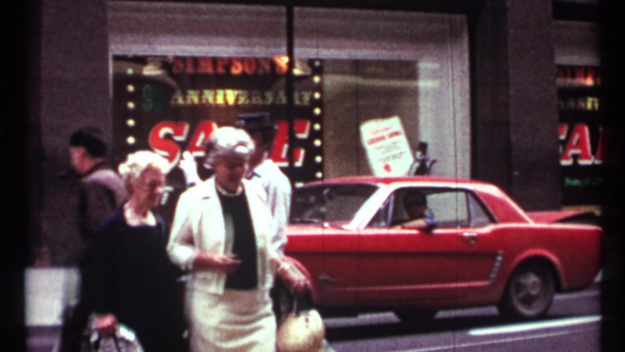 1967 Toronto street view with pedestrians, a storefront anniversary sale sign, and a red Ford Mustang parked at the curb.