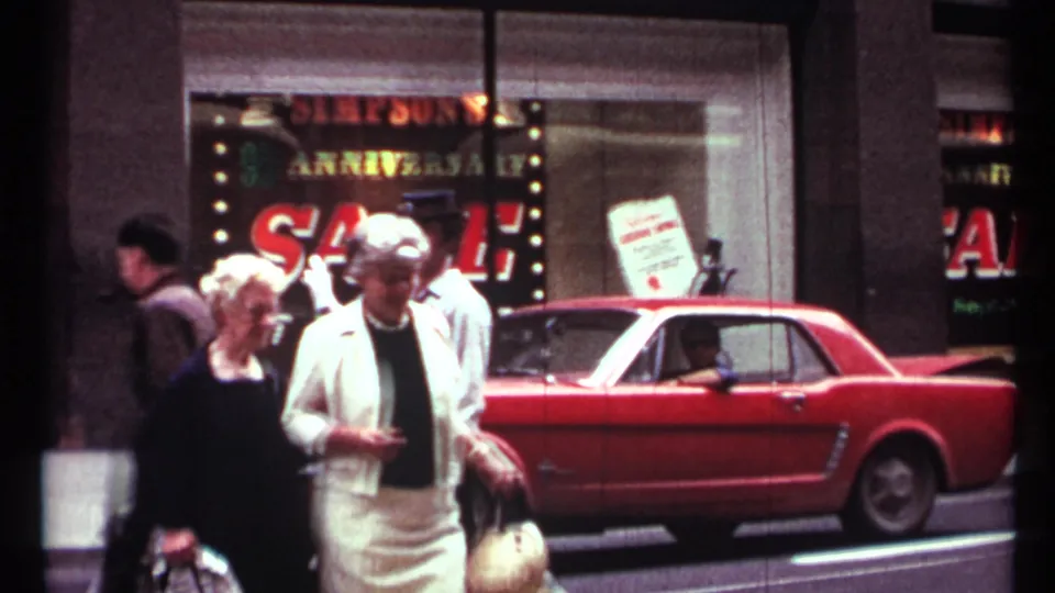 1967 Toronto street view with pedestrians, a storefront anniversary sale sign, and a red Ford Mustang parked at the curb.