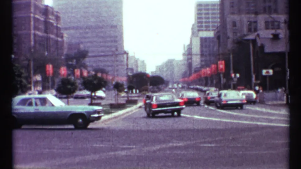 1967 Toronto downtown traffic scene with vintage cars, red street banners, and tall buildings along a broad roadway.