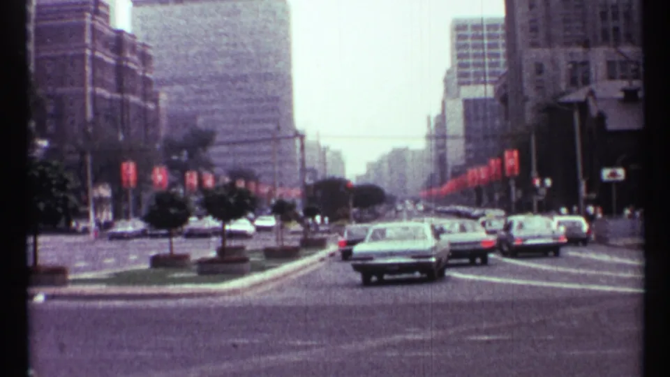 1967 Toronto street view from 8mm footage, showing traffic, a landscaped median, banners, and downtown high-rises.