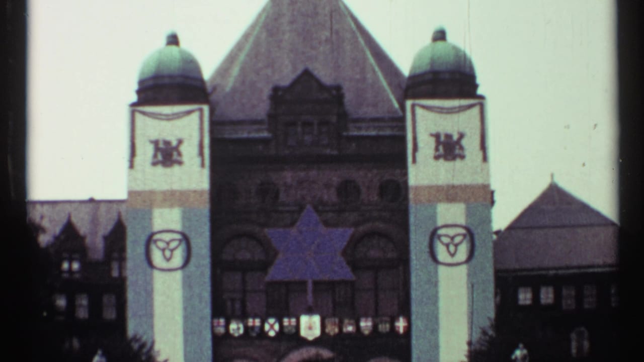1967 Toronto home-movie frame showing a large civic building with tower banners, shields, and a blue star-shaped decoration.