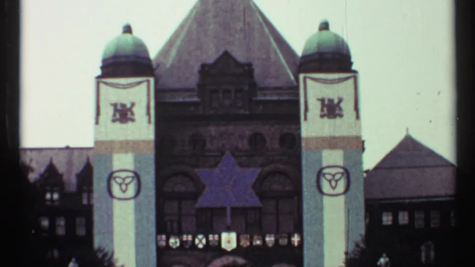 1967 Toronto home-movie frame showing a large civic building with tower banners, shields, and a blue star-shaped decoration.