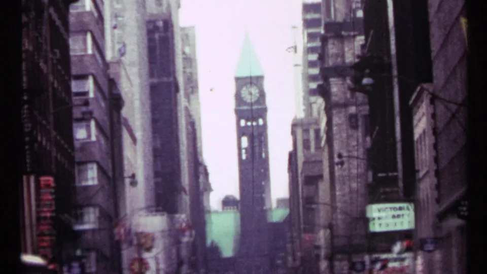 Toronto downtown view showing a clock tower framed by tall buildings, filmed from a narrow street perspective.