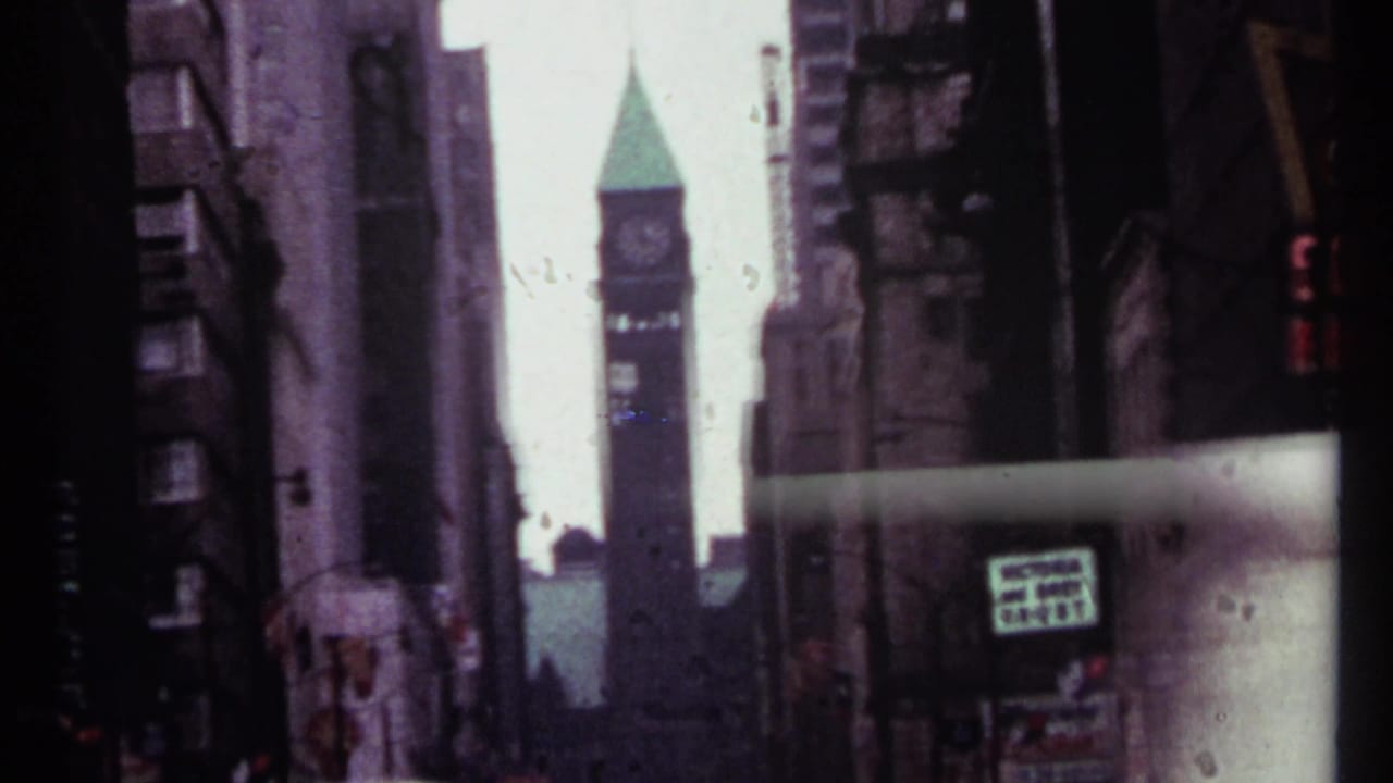Downtown street view with stone buildings, a distant clock tower, and a small visible sign.