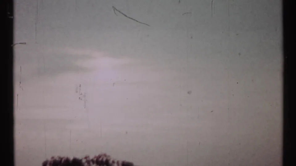 1967 Toronto 8mm frame tilted toward a pale sky with faint flare, scratches, and only the top of foliage visible below.