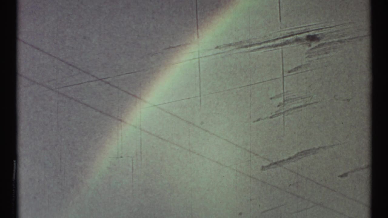 Faint rainbow over a cloudy sky in 1967 8mm footage, with soft fading, grain, and vertical film wear visible.