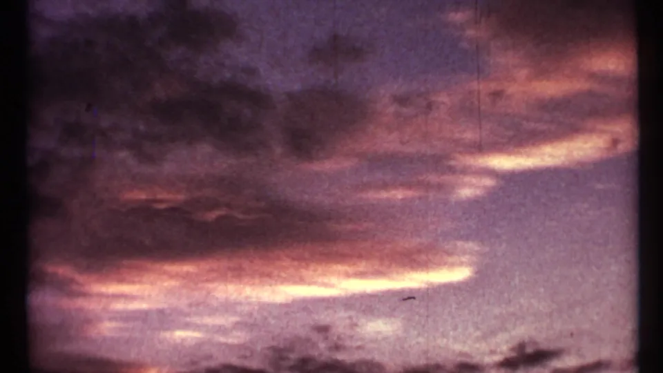 1967 Toronto 8mm frame of a saturated sunset sky with purple clouds, orange highlights, and a dark treeline silhouette.