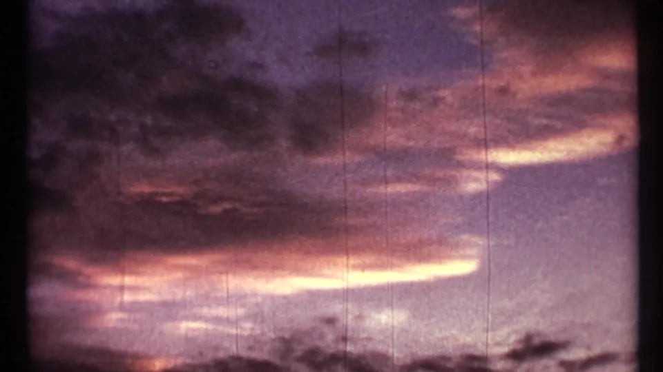 1967 8mm home-movie frame from Toronto showing a dim sunset sky with purple clouds, dark treetop silhouettes, grain, and vertical scratches.