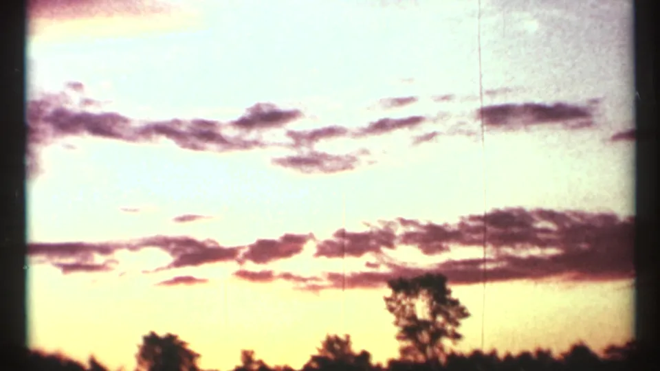 1967 Toronto 8mm frame showing a bright orange-pink sunset behind horizontal cloud bands and a dark line of trees.