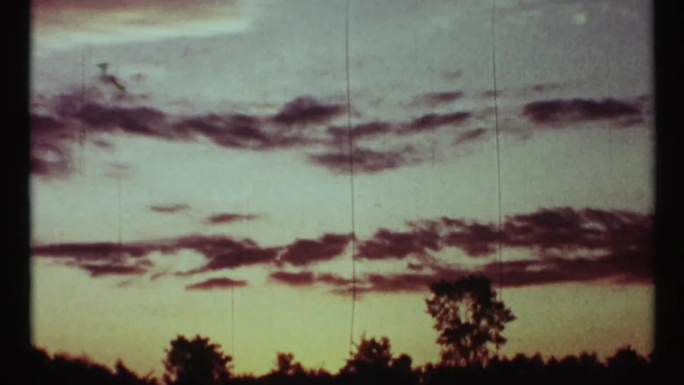 1967 8mm frame from Toronto with a pale blue-green evening sky, dark cloud bands, and treetops silhouetted against the fading light.