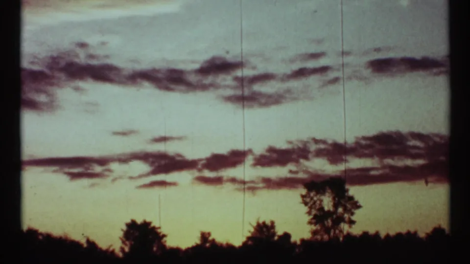 Final 1967 Toronto 8mm frame showing layered clouds above a dark horizon, with a taller tree silhouette near the right edge.