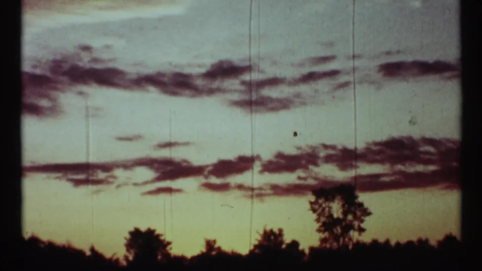 Cloud-streaked dusk sky with silhouetted trees in archival 8mm footage, supported by 1967 Toronto clip metadata.