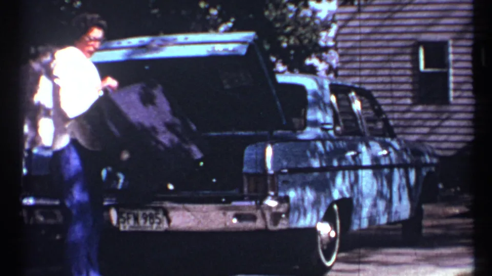 A man handles a suitcase at the open trunk of a classic sedan during a 1967 Toronto home-movie driveway shot.