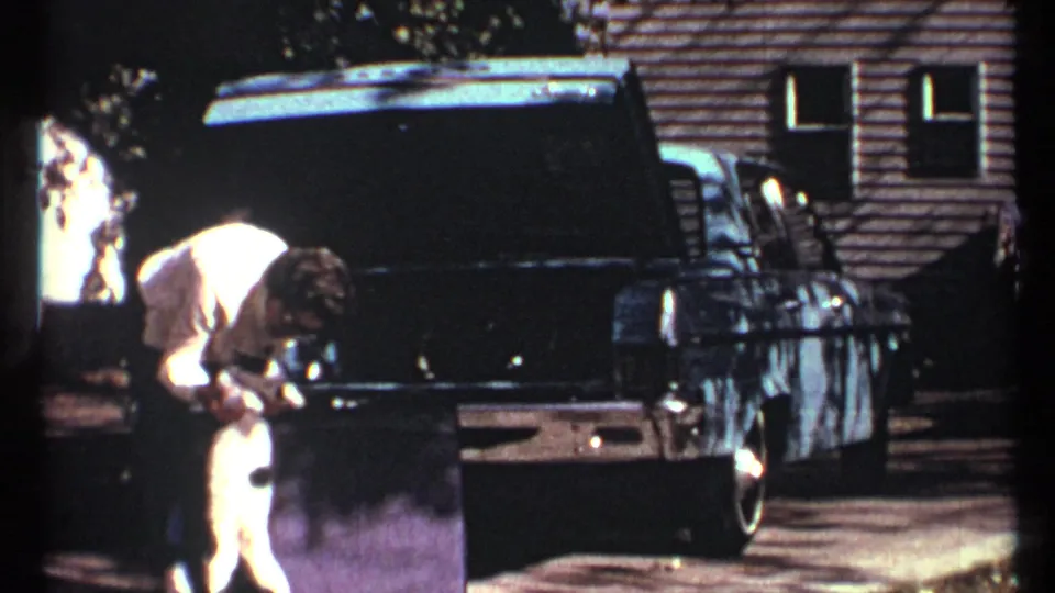 The woman appears to pet or steady the white cat beside the open trunk of the dark sedan in a Toronto driveway scene.