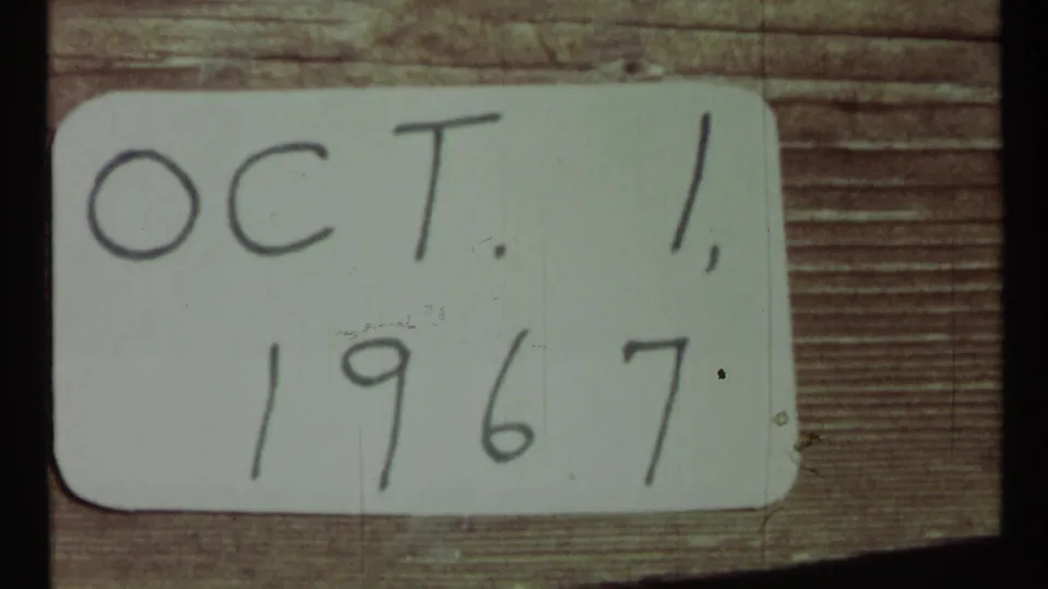 Close 8mm frame of a handwritten Oct. 1, 1967 card against wood, with soft focus and visible film wear.