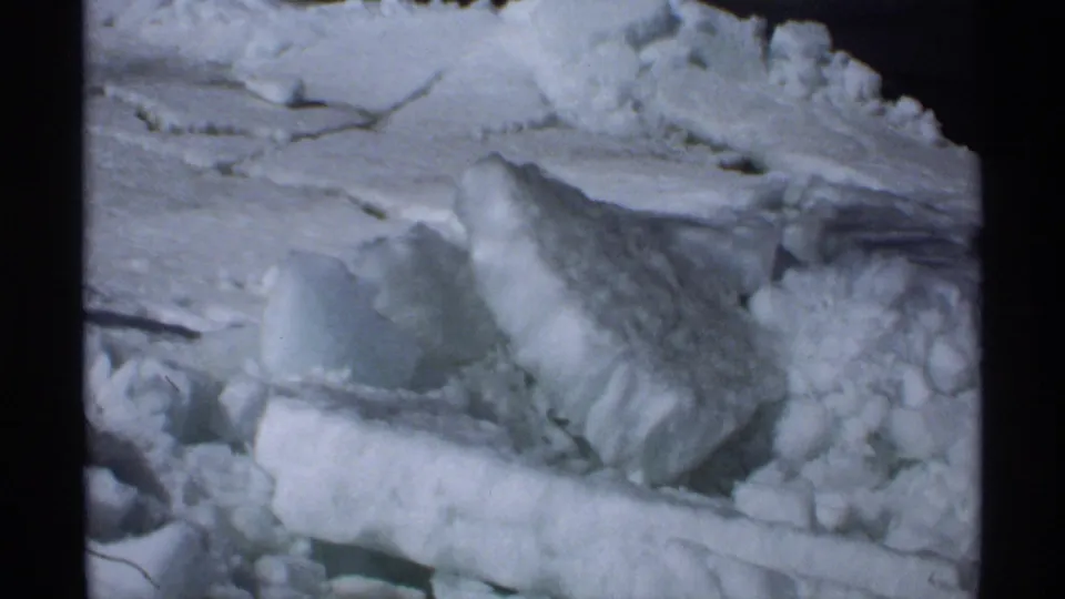 1970 Minnesota 8mm frame showing a close view of packed snow, broken ice, and rough winter buildup near a roadside.