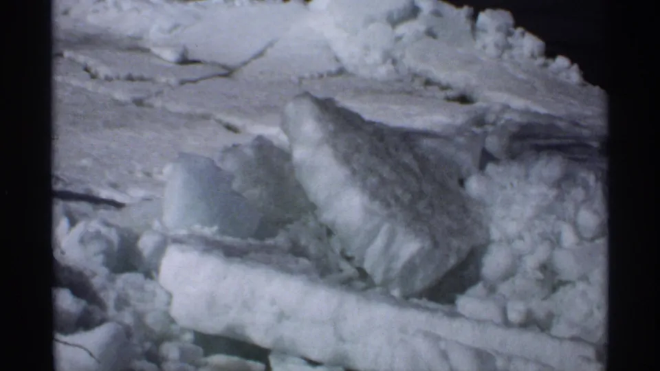 1970 Minnesota home-movie frame with uneven snow slabs and ice chunks filling most of the view.