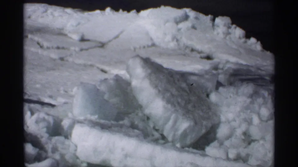 Vintage 8mm frame from Minnesota showing packed roadside snow and broken ice in a tight winter close-up.