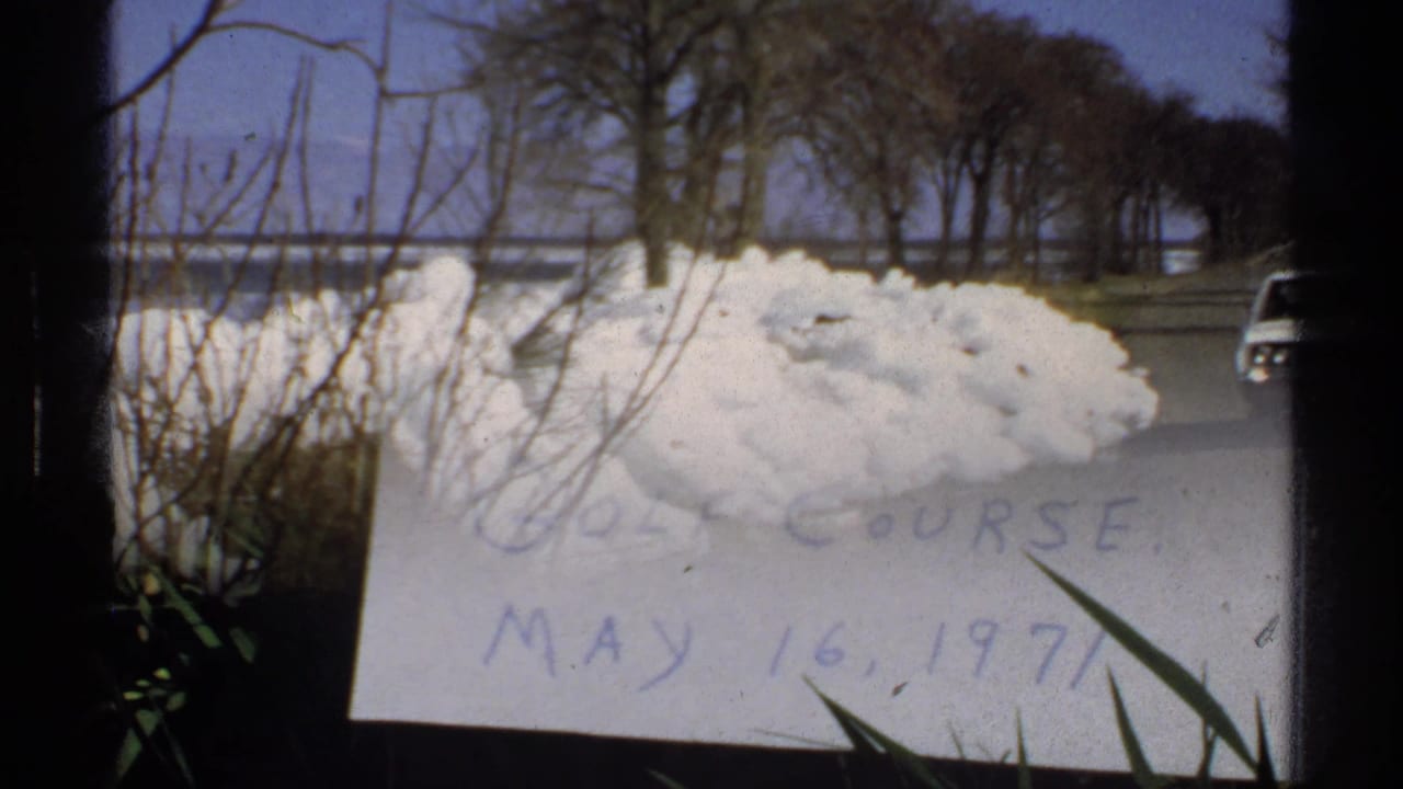 Snow piled beside a quiet road with bare trees and water in the distance.