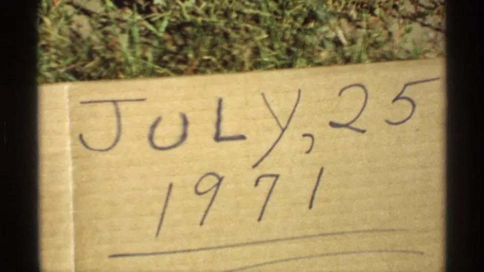Handwritten cardboard date card on grass reading July 25, 1971, filmed as part of the 8mm home-movie record.