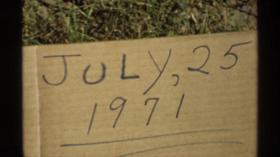 Minnesota 8mm frame showing a cardboard date card marked July 25, 1971, set against grass with dark film borders.