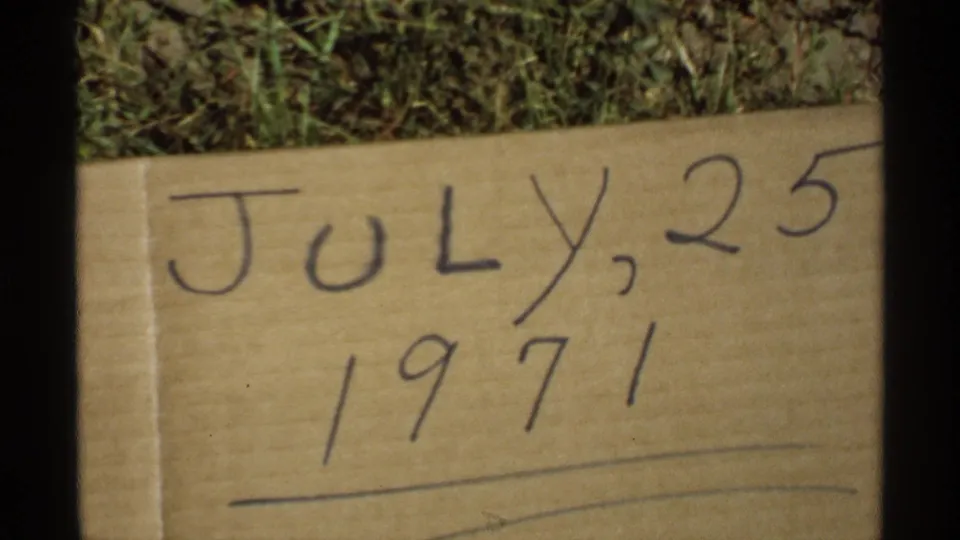 A second 8mm frame of the handwritten July 25, 1971 cardboard marker, with grass visible above and film-frame borders at the sides.