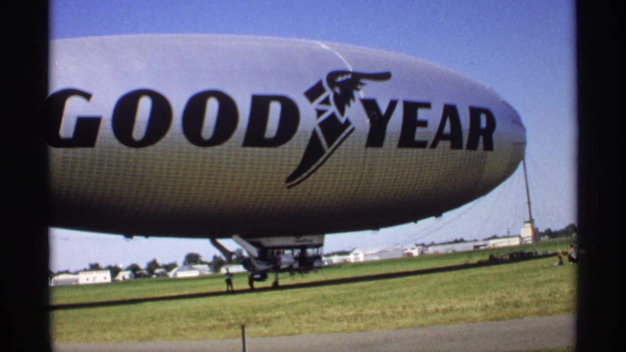 Close view of a Goodyear blimp on a grassy field under a blue sky.