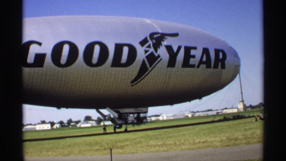 Minnesota 1970 8mm frame showing the Goodyear blimp side with large black logo lettering, gondola area and grassy airfield.