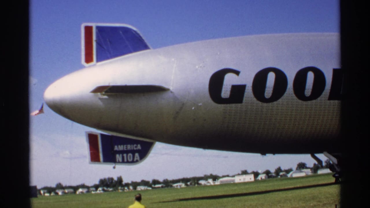 Close view of a silver Goodyear blimp nose over a grassy airfield.