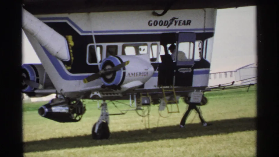 1970 Minnesota home-movie frame of a blue-and-white Goodyear marked aircraft section resting on a grassy airfield.