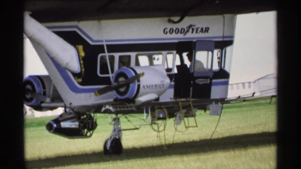 1970 Minnesota home-movie frame showing the Goodyear aircraft section, landing gear, and a man near the doorway.