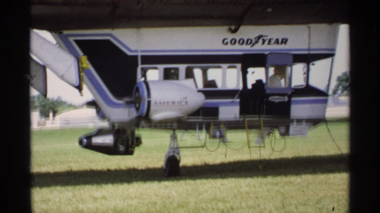 Goodyear blimp gondola and landing gear on a grass field.