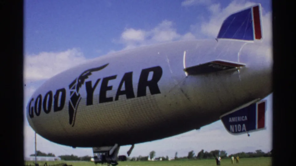 1970 Minnesota 8mm close view of the Goodyear blimp body and tail section, with large logo lettering against a blue sky.