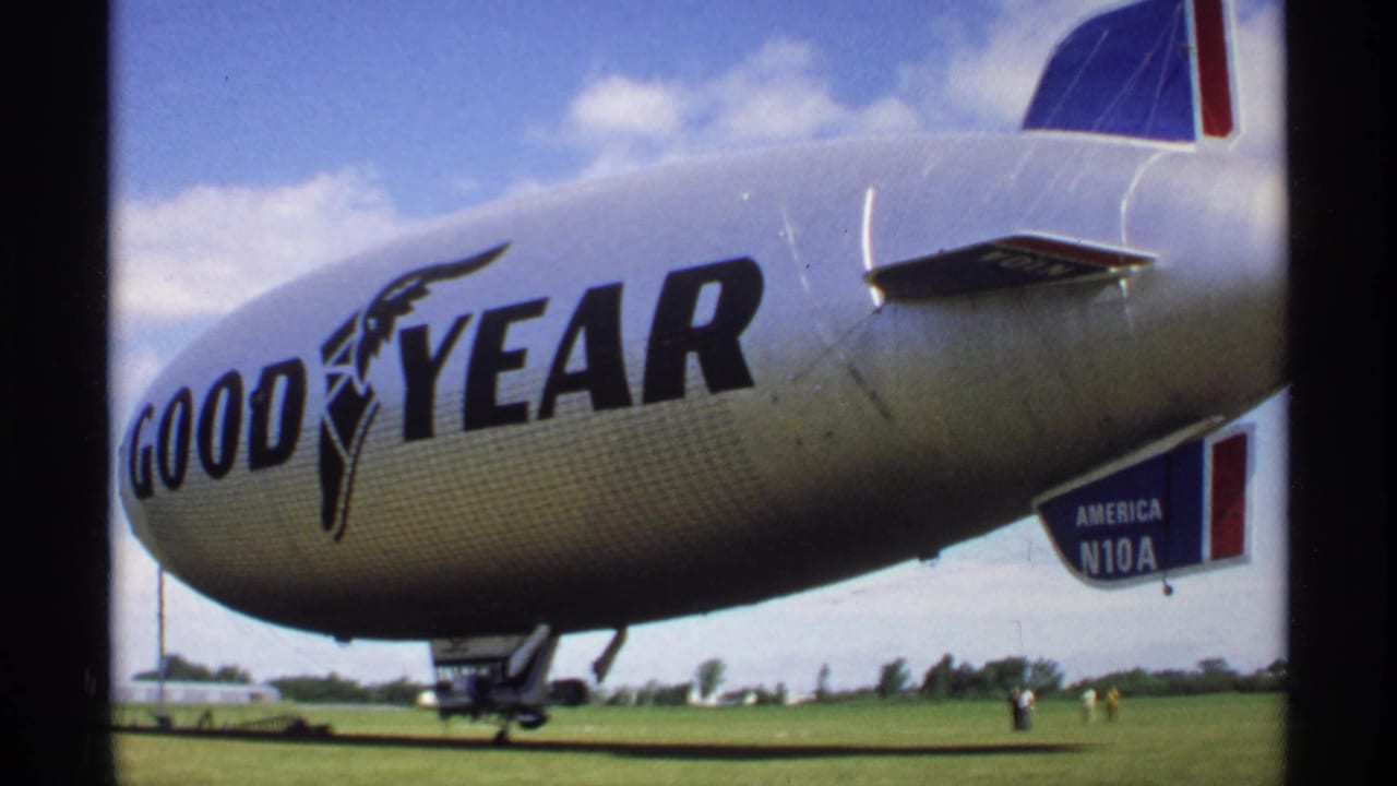 Goodyear blimp on a grassy airfield with large logo and tail marking visible.