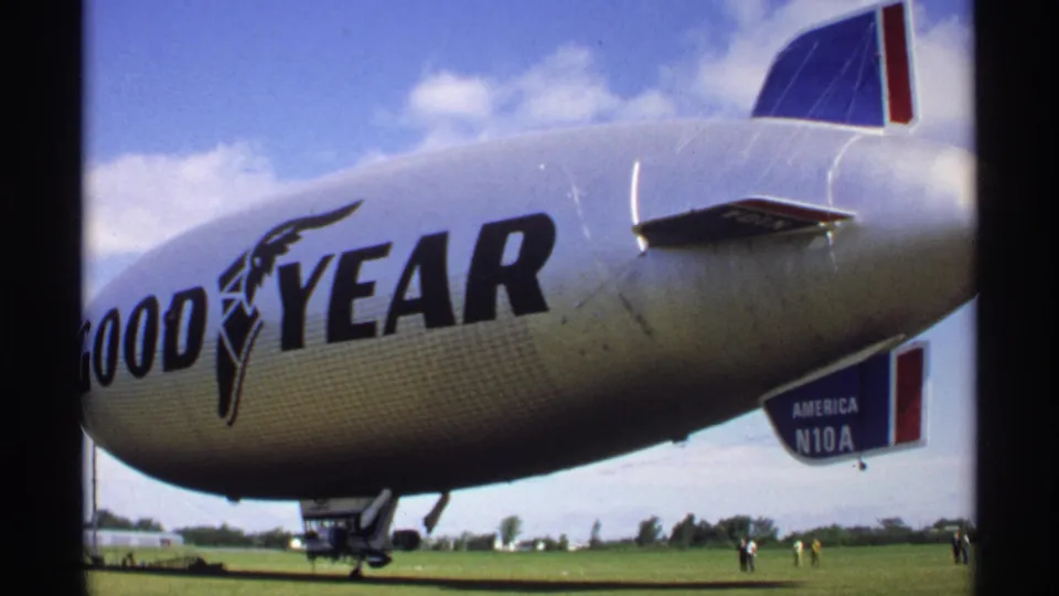 The Goodyear blimp America N10A appears grounded on a Minnesota airfield, with people small in the distance.