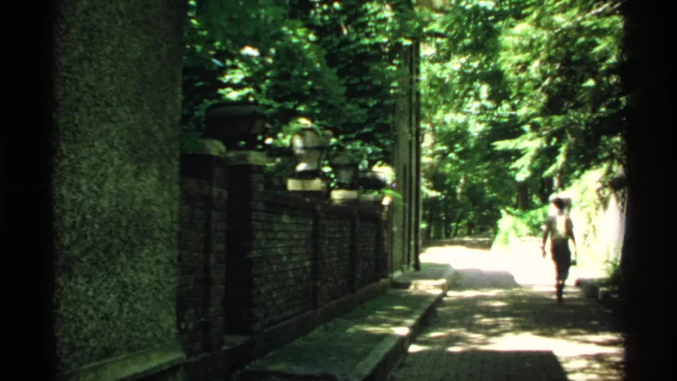 1970 Minnesota 8mm frame showing an adult man walking away on a brick path beside a wall and ornamental garden urns.