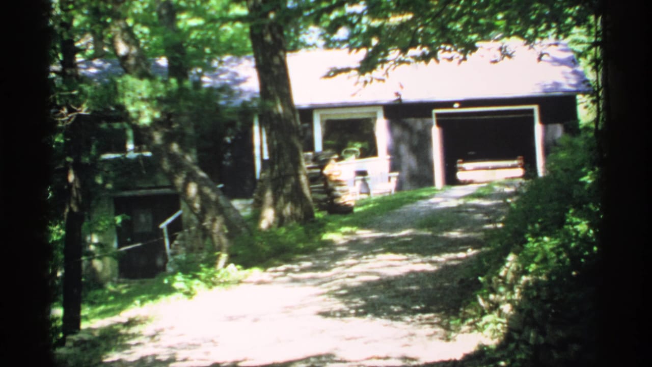 Tree-lined dirt driveway leading toward a dark house with an open garage.